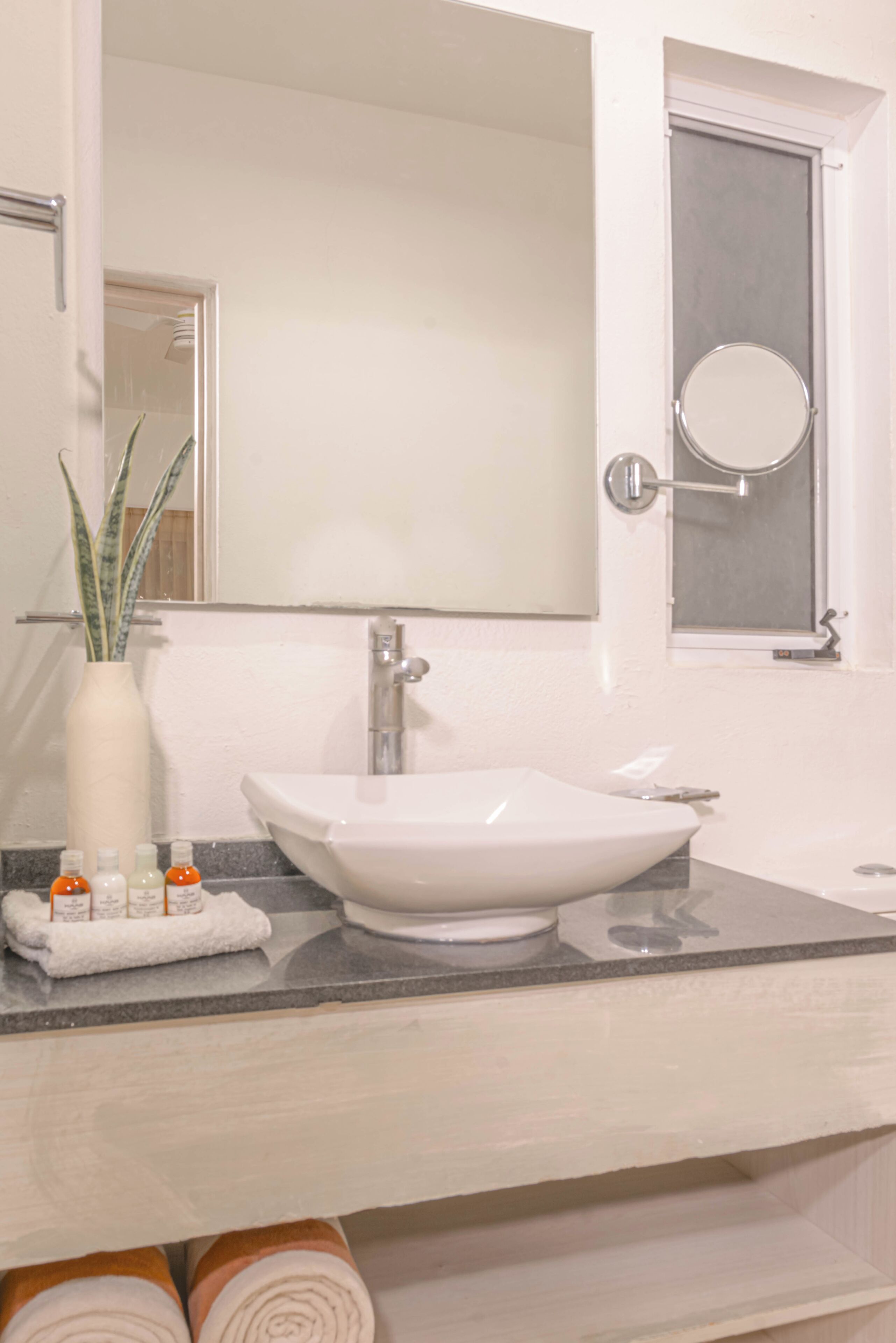 Un baño con lavamanos blanco, espejo, toallero y ventana con puerta de vidrio esmerilado.