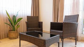 Una silla de mimbre y una mesa con superficie de vidrio en una habitación con cortinas y una planta en maceta.