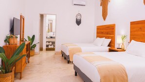 Habitación de hotel con dos camas, televisión, cabecero de madera, aire acondicionado instalado en la pared y un pasillo que conduce a un baño.