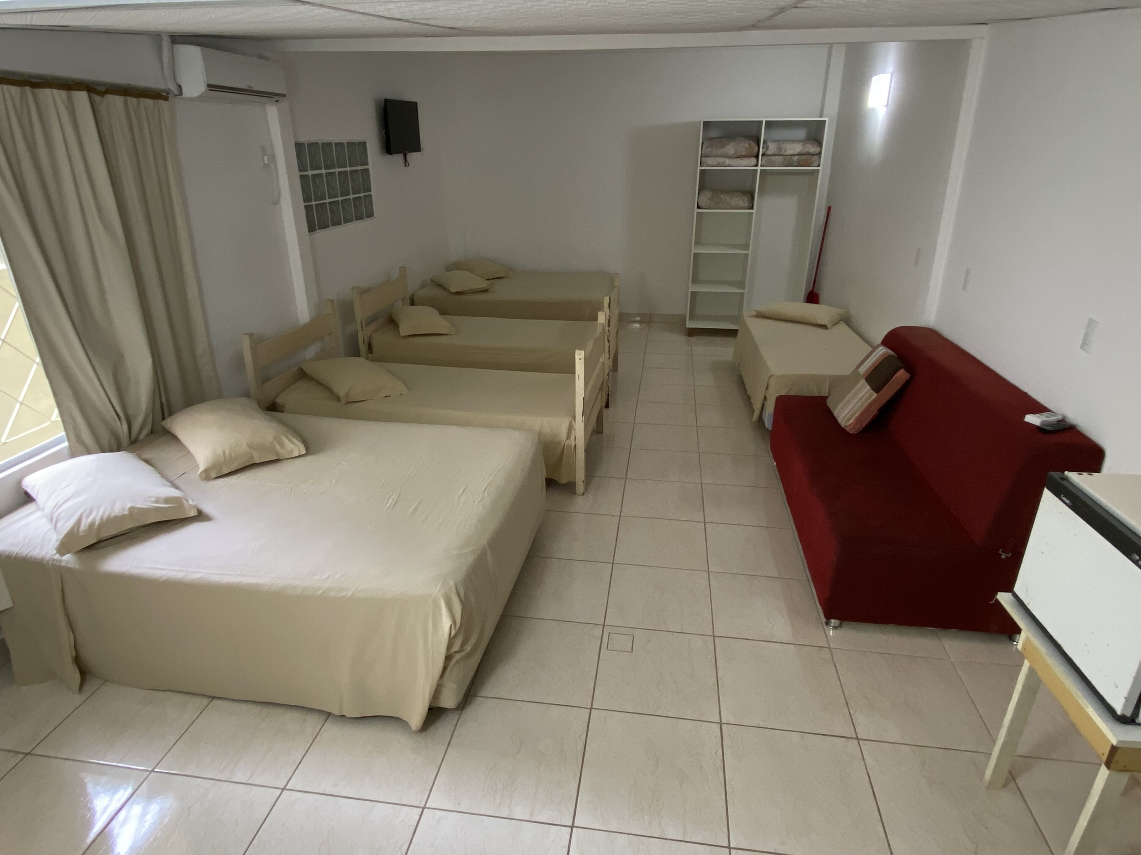 Une chambre d’hôtel avec quatre lits, un canapé rouge, un bureau et une armoire.
