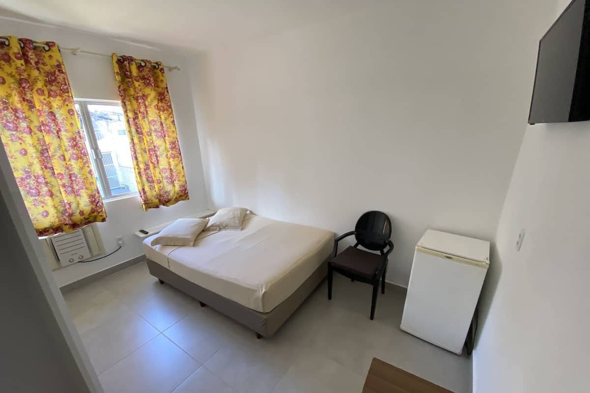 Un dormitorio con una cama, una silla, una mesita y un refrigerador.