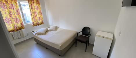 Une chambre à coucher avec un lit, une chaise, une petite table et un réfrigérateur.