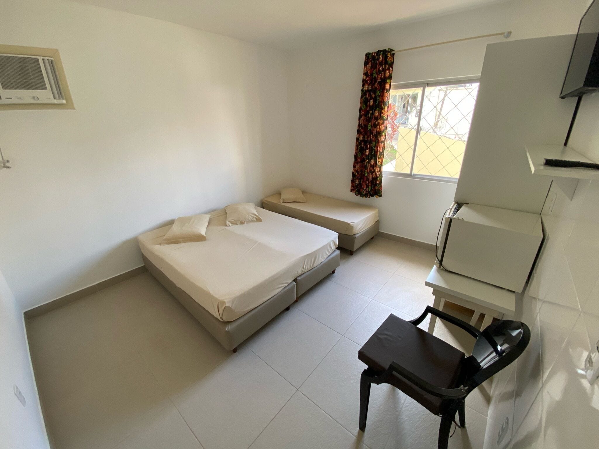 A small, clean room with a bed, a desk, and a window with curtains.