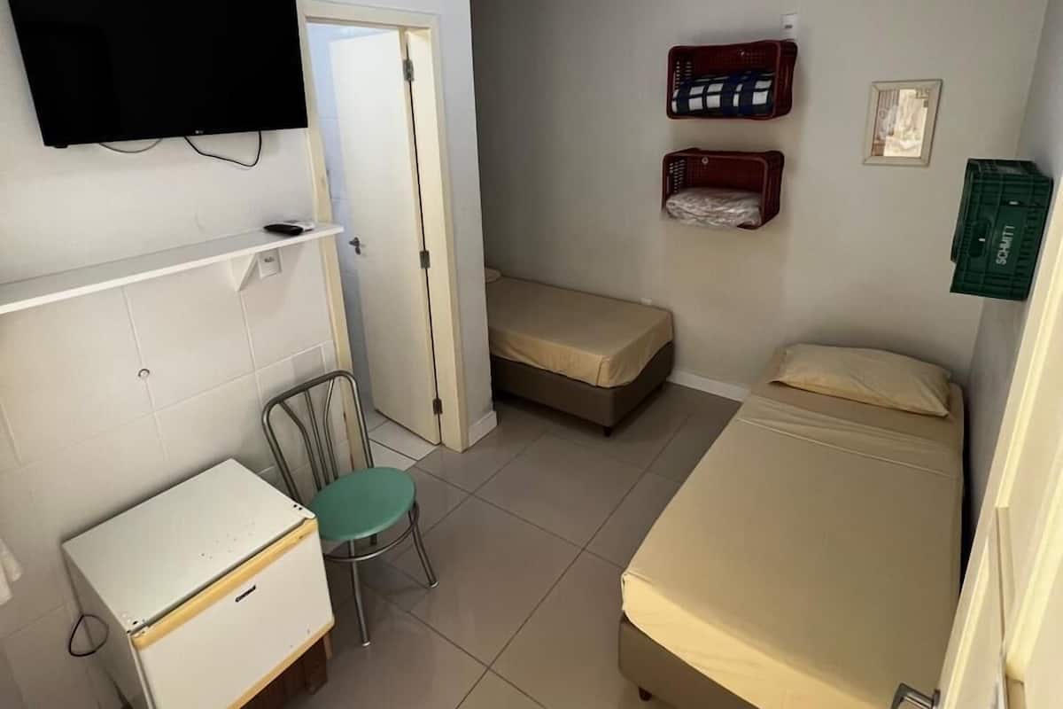 Una habitación pequeña y limpia con una cama, un escritorio, una silla, un televisor y un calentador fijado a la pared.