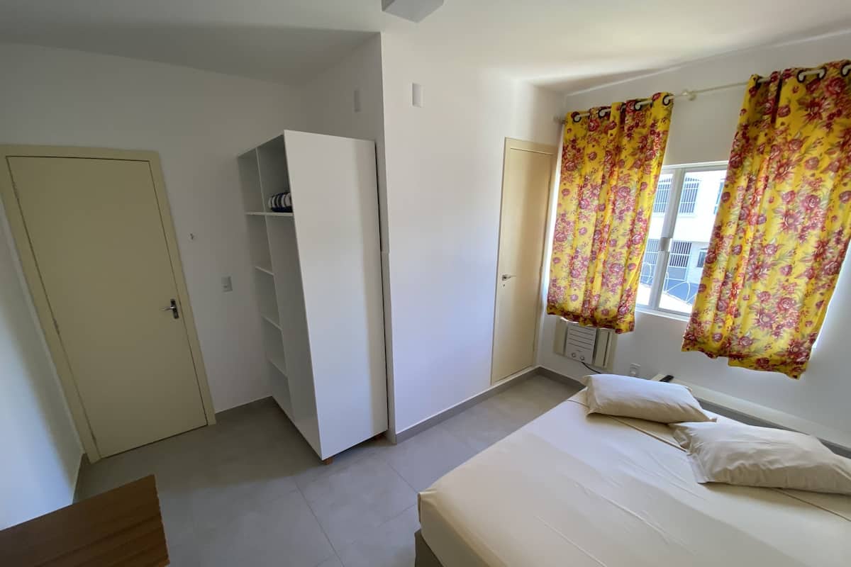 Un dormitorio con cama, armario, escritorio y ventana con cortinas.