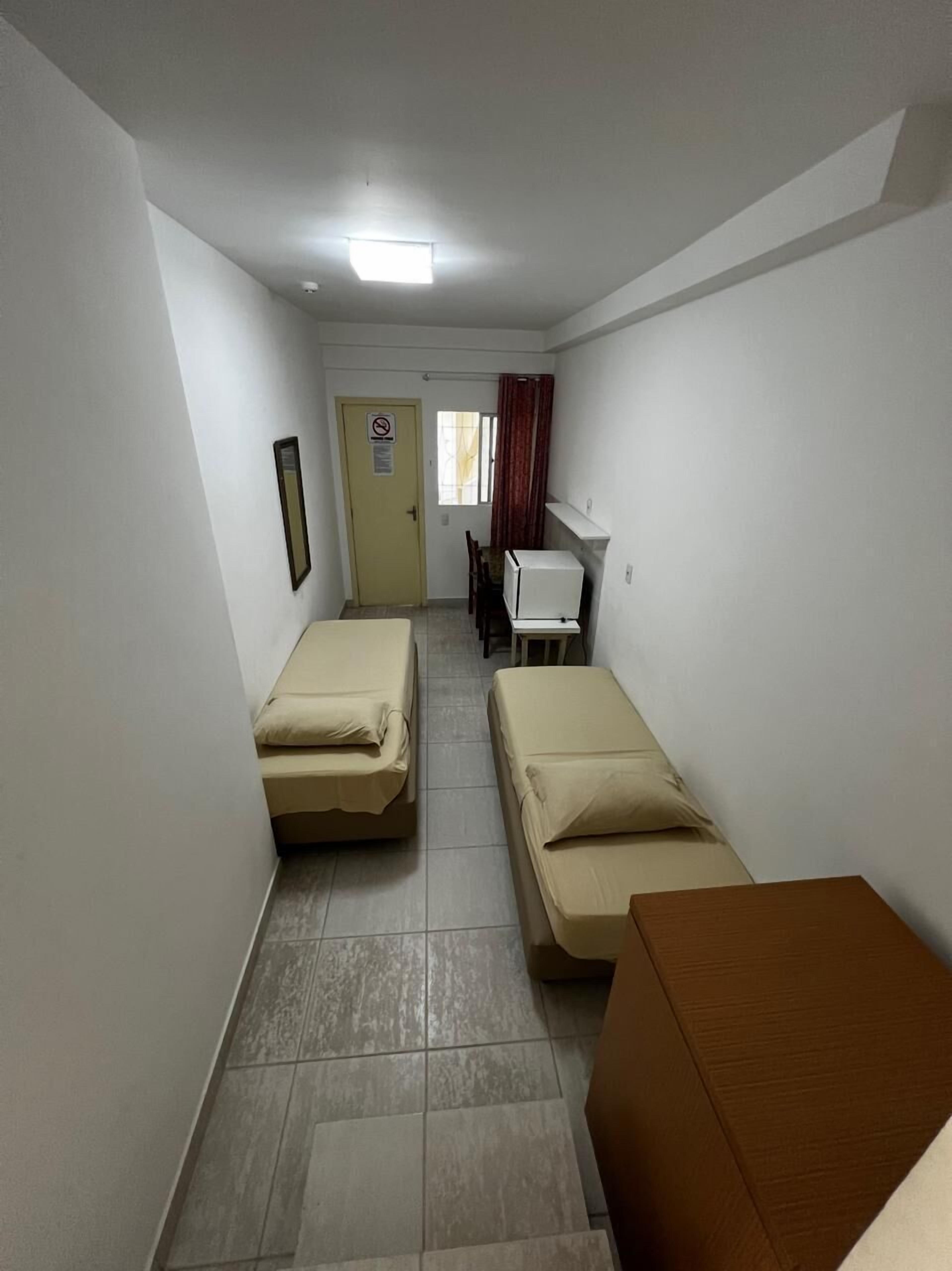 A narrow hallway with two single beds, a desk, and a chair.