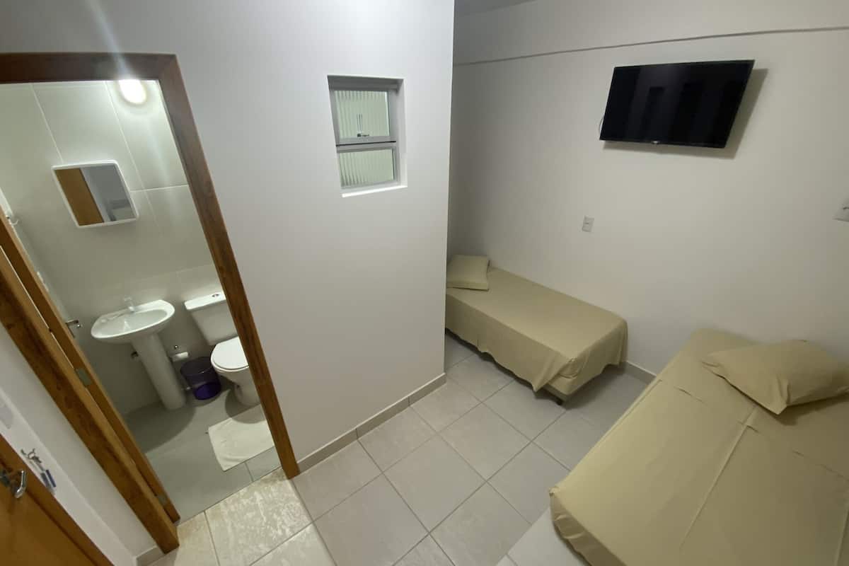 Una habitación pequeña con cama, televisor, ventana y baño con lavamanos e inodoro.