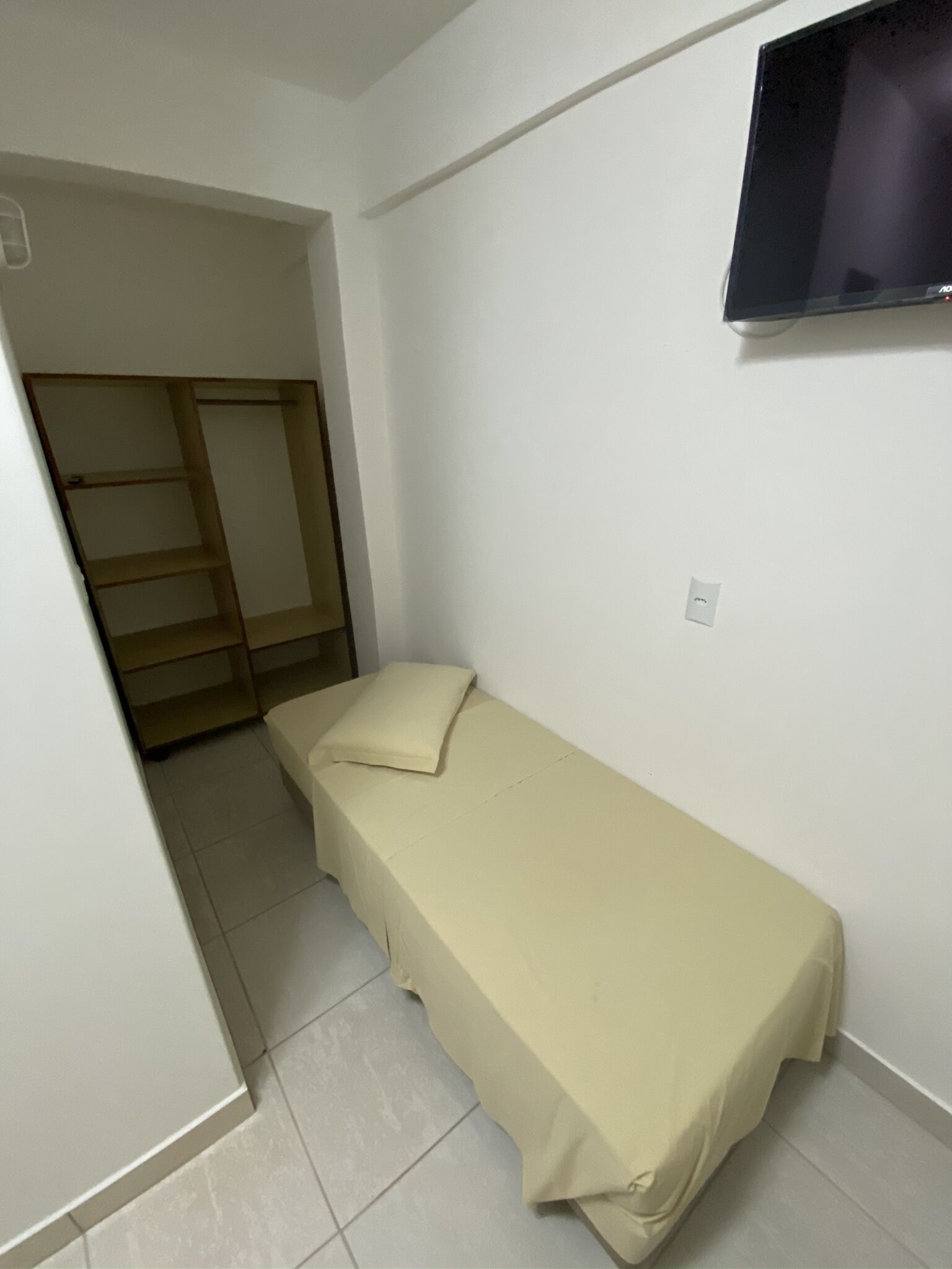 Een kleine kamer met een enkel bed en een televisie aan de muur.