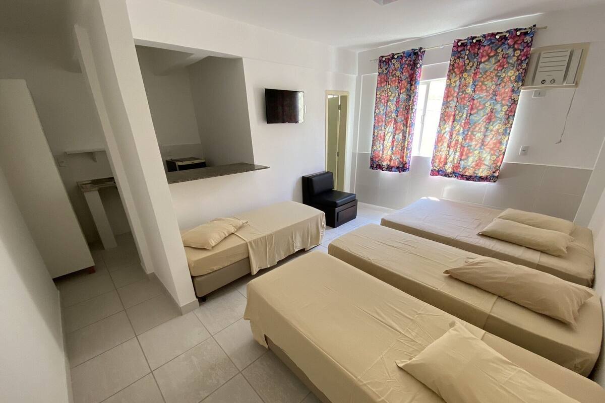 Habitación de hotel con tres camas, un escritorio pequeño, un espejo y un televisor.