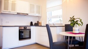 Une cuisine moderne avec des meubles blancs, un four encastré, une machine à café et une fenêtre donnant sur un beau paysage.