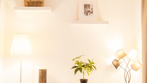 Une commode blanche, sur laquelle sont posés un pot de fleurs, un tableau encadré et une lampe sur pied.