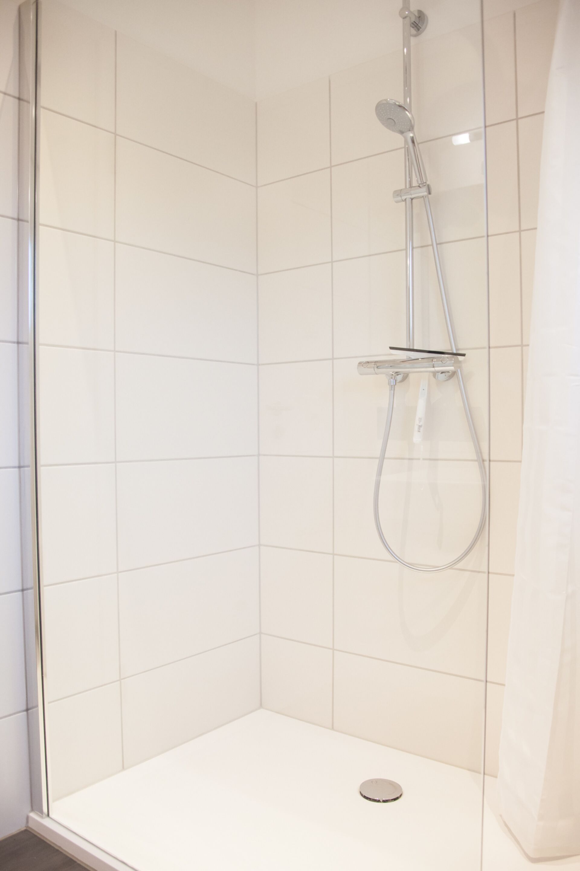 Une cabine de douche moderne dotée d’une porte en verre, d’un pommeau de douche à main et d’un robinet mural.