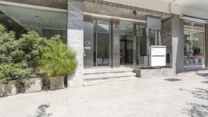 Une entrée moderne avec des portes en verre, une façade en marbre et un petit espace extérieur aménagé avec des plantes.