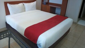 A neatly made bed with white and red bedding, a wooden headboard, and a small table with a patterned tablecloth. - Daiichi Hotels (Isiolo)