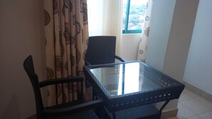 A small room with a glass-top table and two chairs, a window with curtains, and a red blanket on the floor. - Daiichi Hotels (Isiolo)
