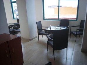 Una habitación con una mesa y sillas de vidrio, vistas a edificios exteriores y suelo de baldosas.