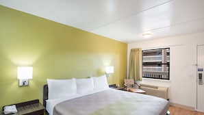 A hotel room with a bed, nightstand, lamp, chair, and window with curtains. - Studio 6 - Colorado Springs - Air Force Academy  (Colorado Springs)