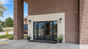 A building entrance with a brick facade, glass doors, and two wall-mounted lights. - Studio 6 - Colorado Springs - Air Force Academy  (Colorado Springs)