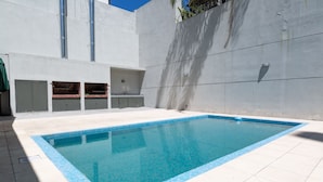 Una piscina rectangular con borde de azulejos, rodeada de una terraza con baldosas blancas.