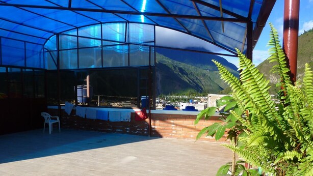 A covered outdoor area with a table and chairs, a potted plant, and a view of a mountainous landscape. - Hostal Nomada - Hostel (Baños de Agua Santa)