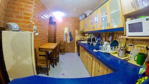 A compact kitchen with a brick wall, wooden cabinets, a blue countertop, and a microwave. - Hostal Nomada - Hostel (Baños de Agua Santa)
