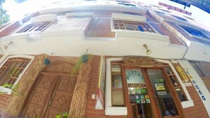 A building with a reception area, a sign reading "Hostal Nomada," and a window with a view of the street. - Hostal Nomada - Hostel (Baños de Agua Santa)