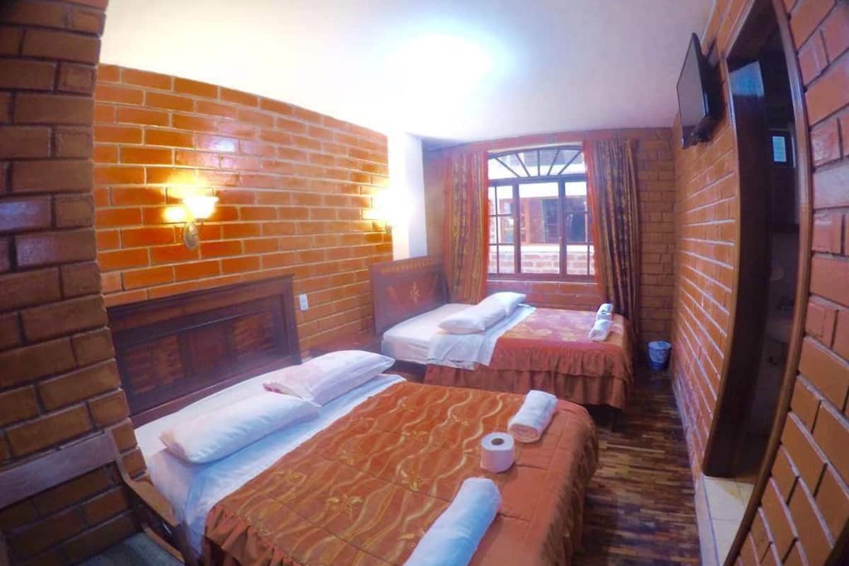 Une chambre avec deux lits, chacun doté d’une tête de lit, une fenêtre avec des rideaux et un mur en briques.