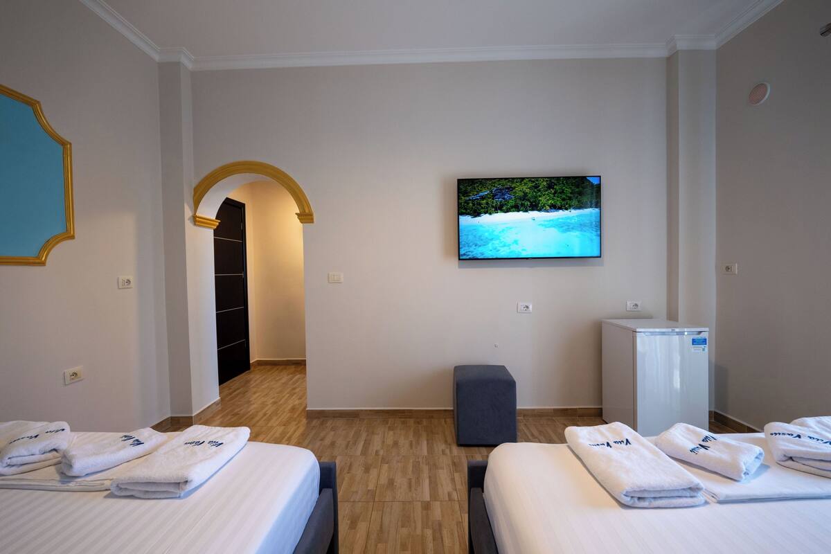 Habitación de hotel con dos camas, un televisor en la pared, un escritorio pequeño y una puerta que da a un pasillo.