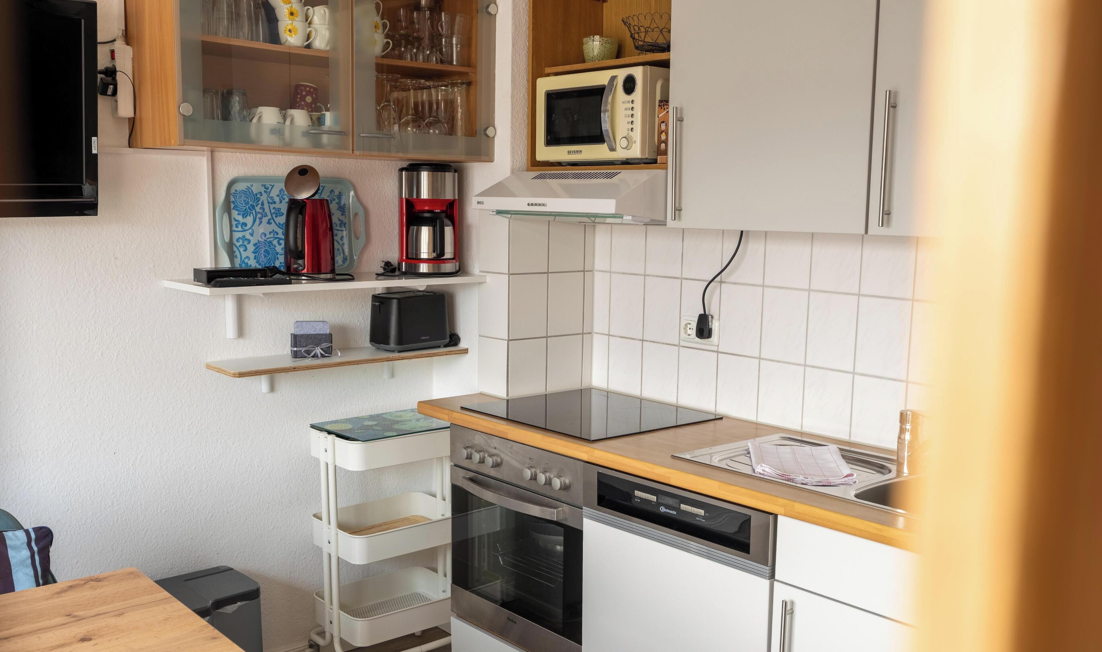 A compact kitchen with a microwave, toaster, and oven. There are shelves above the counter holding various kitchen items.