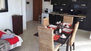 A dining area with a table set for four, surrounded by wicker chairs. A washing machine is visible in the background, and a microwave is on the counter. - Boa Vista Holidays (Boa Vista)