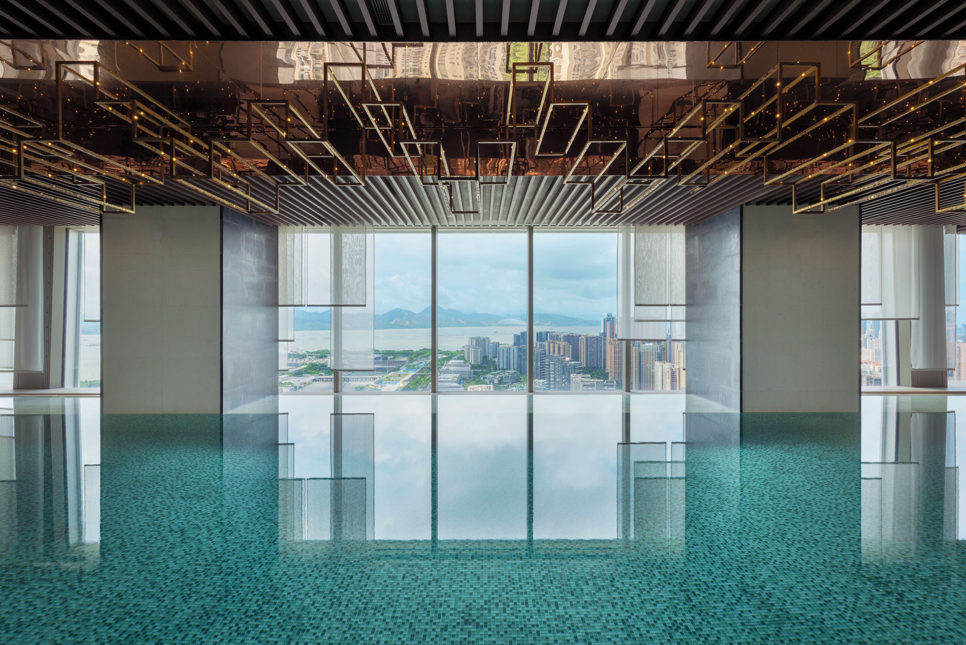 A spacious indoor area with a large window offering a city view, a reflective floor, and a modern ceiling design.