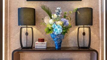 A room with a marble wall, a blue vase with flowers, two black lamps, and a small stack of books.