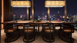Un comedor moderno con vistas a la ciudad, que presenta una mesa larga con sillas y lámparas colgantes.