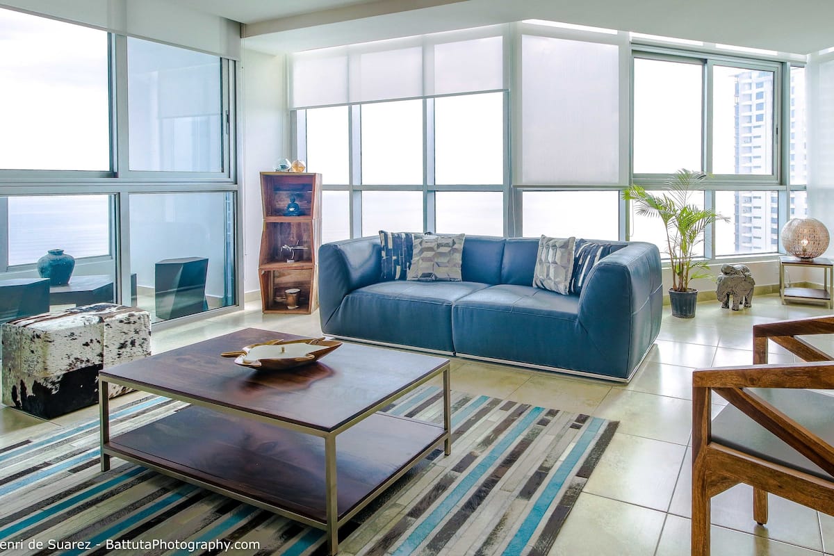 Uma sala de estar espaçosa com um sofá azul, mesa de centro de madeira e um tapete listrado.