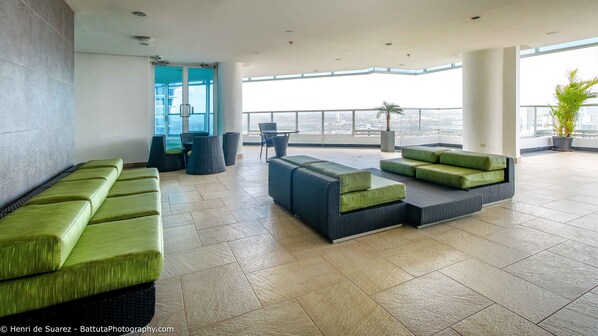 A modern lounge area with green and black seating, a glass door, and a view of the city.