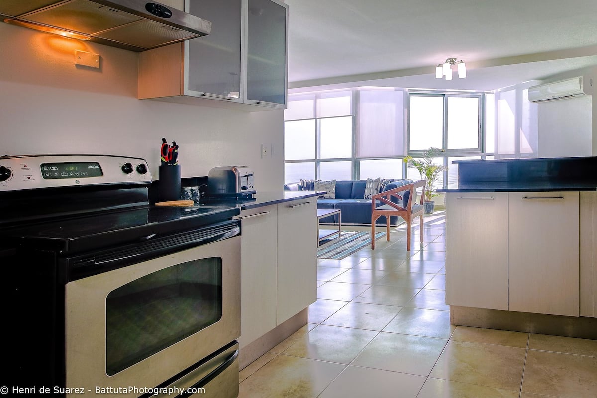 Cozinha equipada com fogão, micro-ondas e torradeira. Zona de refeições com mesa e cadeiras.