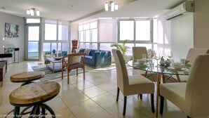 A spacious living area with a glass dining table, comfortable seating, and large windows offering a view.
