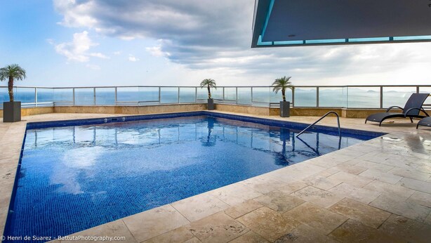 An indoor swimming pool with clear blue water, a tiled floor, and a view of the ocean through a glass barrier.