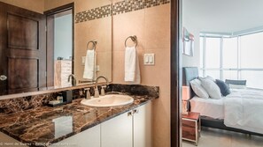 A modern bathroom with a marble countertop, a sink, and a large mirror. There are two towels hanging on towel rings.