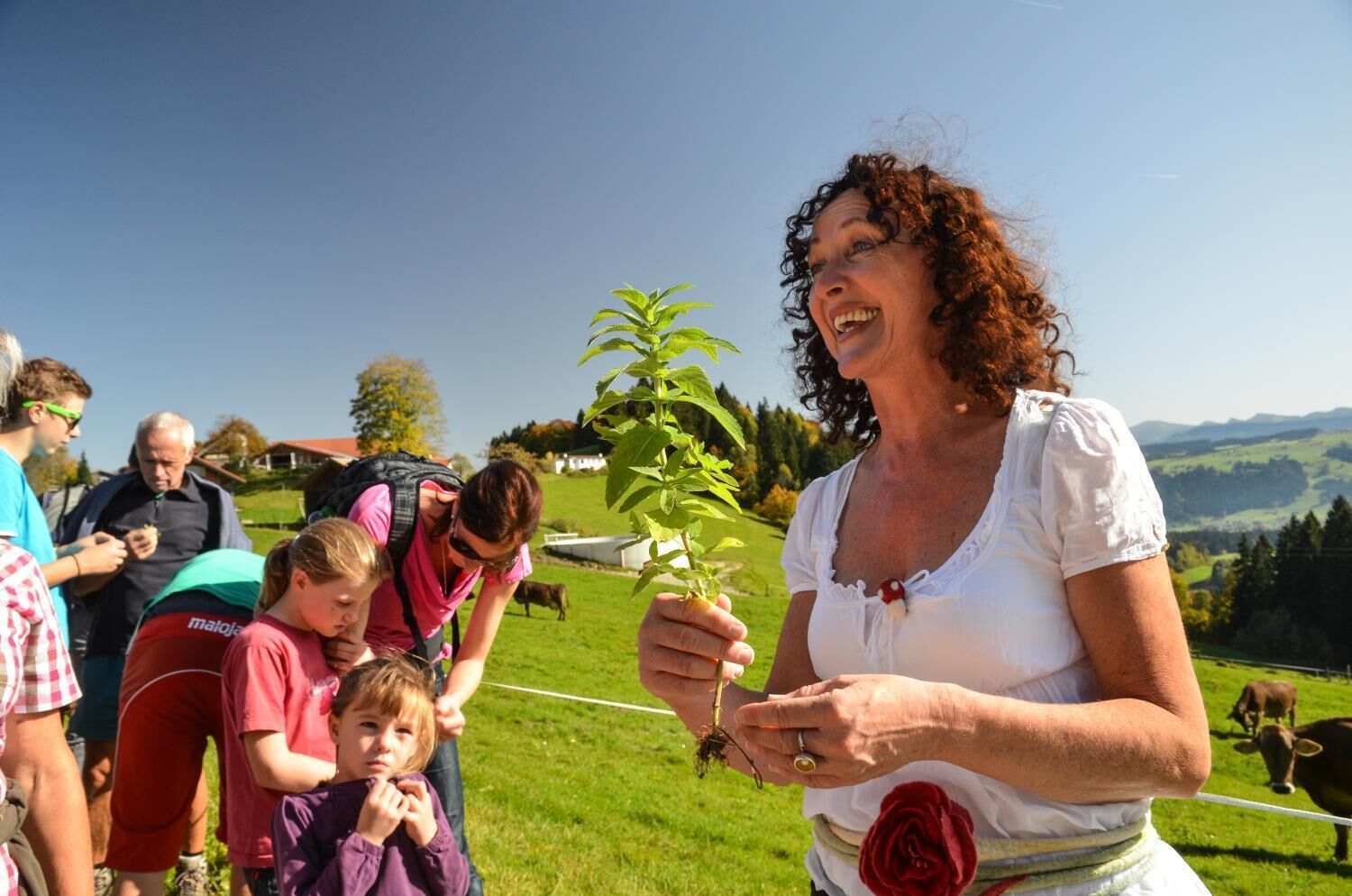 A woman holding a plant with a rural landscape in the background.