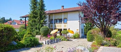 A two-story building with a tiled roof, surrounded by lush gardens and a chessboard.