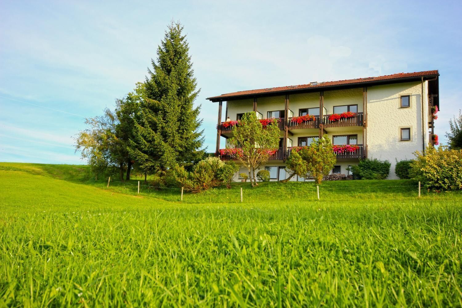 Un hotel con una estructura de varios pisos, balcones con jardineras de flores y un césped verde exuberante.