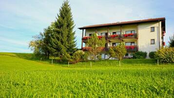 Ein Hotel mit mehrgeschossiger Bauweise, Balkonen mit Blumenkästen und einem üppigen Rasen.