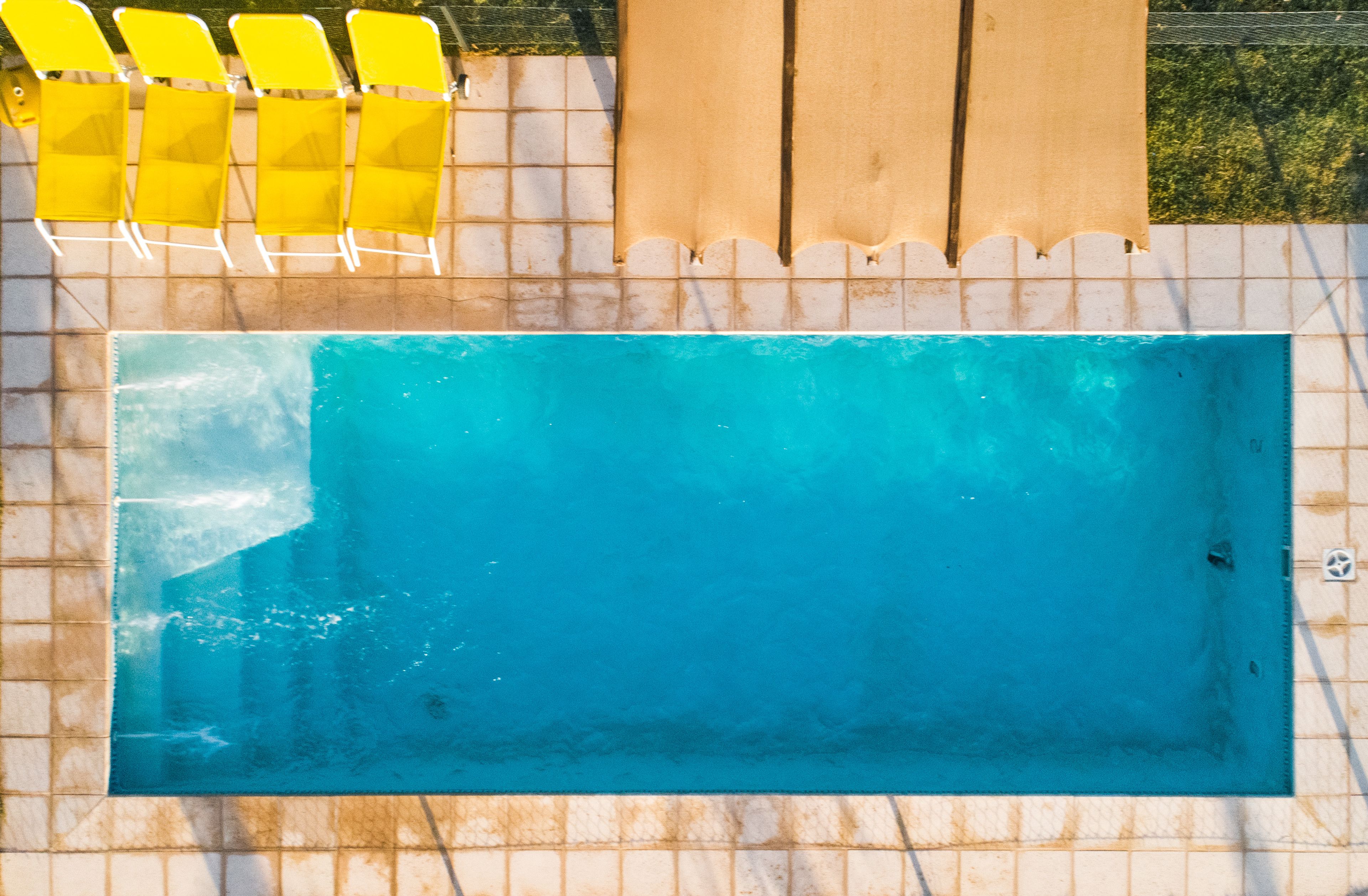 A rectangular swimming pool with a tiled deck and yellow chairs.