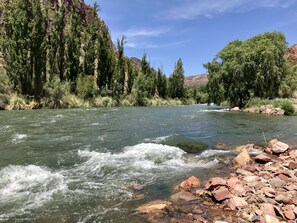 A river with clear water flowing through a rocky bed, surrounded by dense green trees and hills in the background. - Cabañas EcoNature (San Rafael)