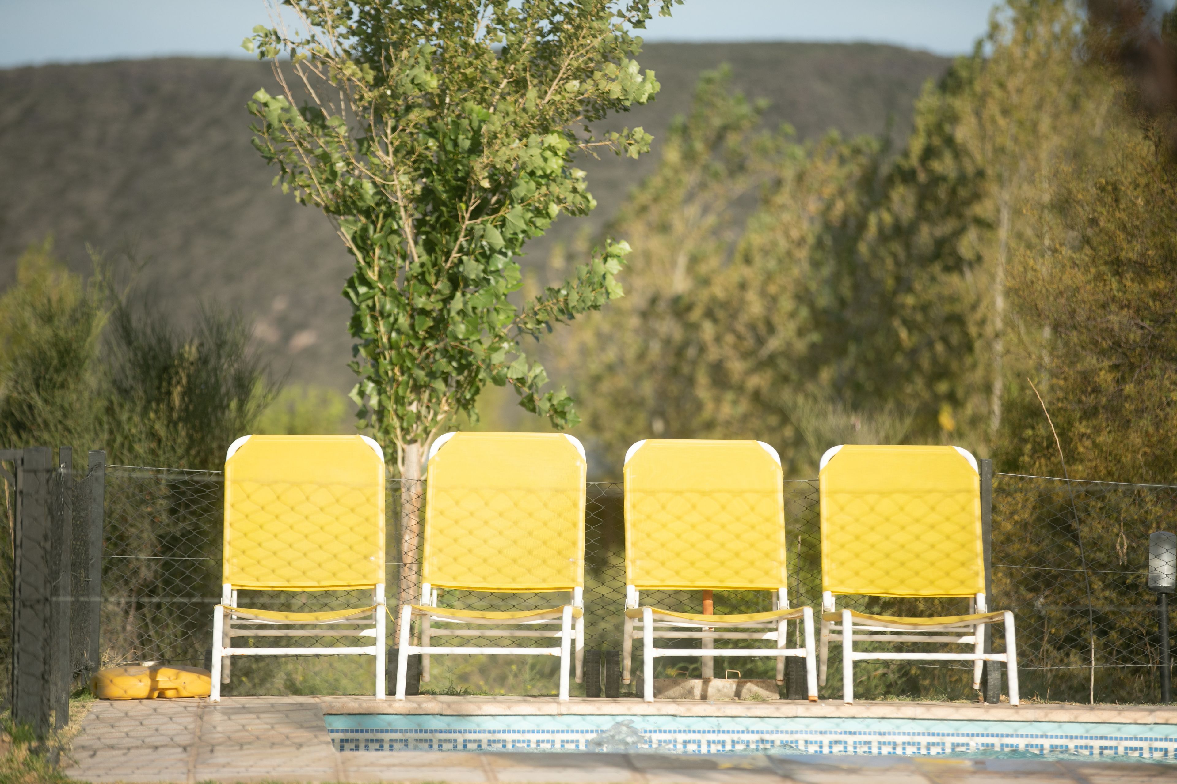 Trois chaises jaunes à ossature blanche, avec une piscine en arrière-plan.