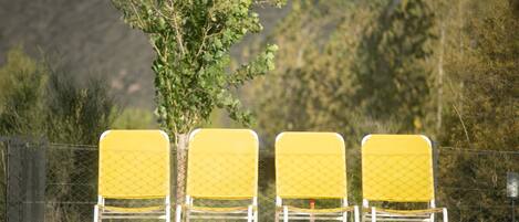 Trois chaises jaunes à ossature blanche, avec une piscine en arrière-plan.