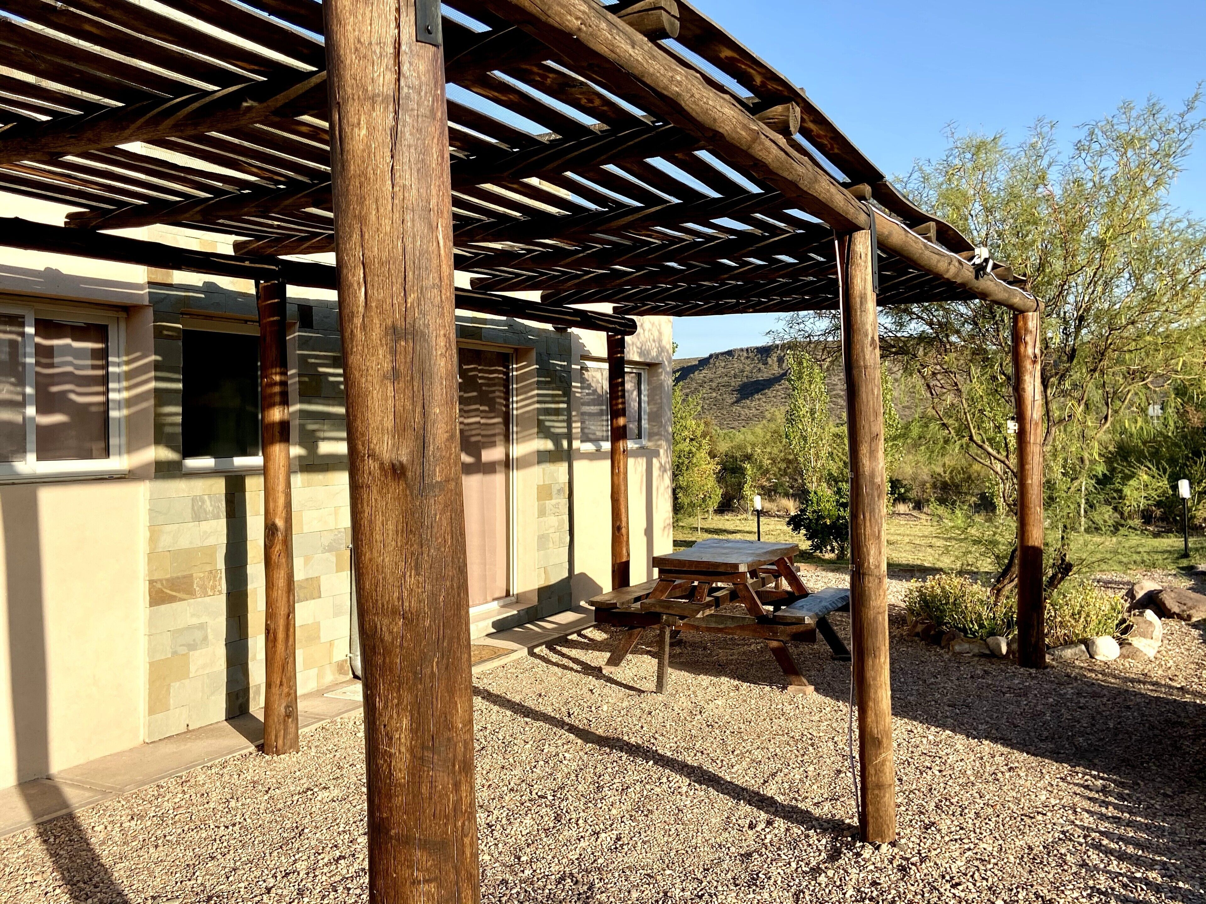 Un patio cubierto con una pérgola de madera, paredes de piedra y suelo de grava.