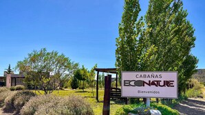 Letrero que dice "CABANAS ECONATURE" con un mensaje de bienvenida, rodeado de follaje y un cielo despejado.