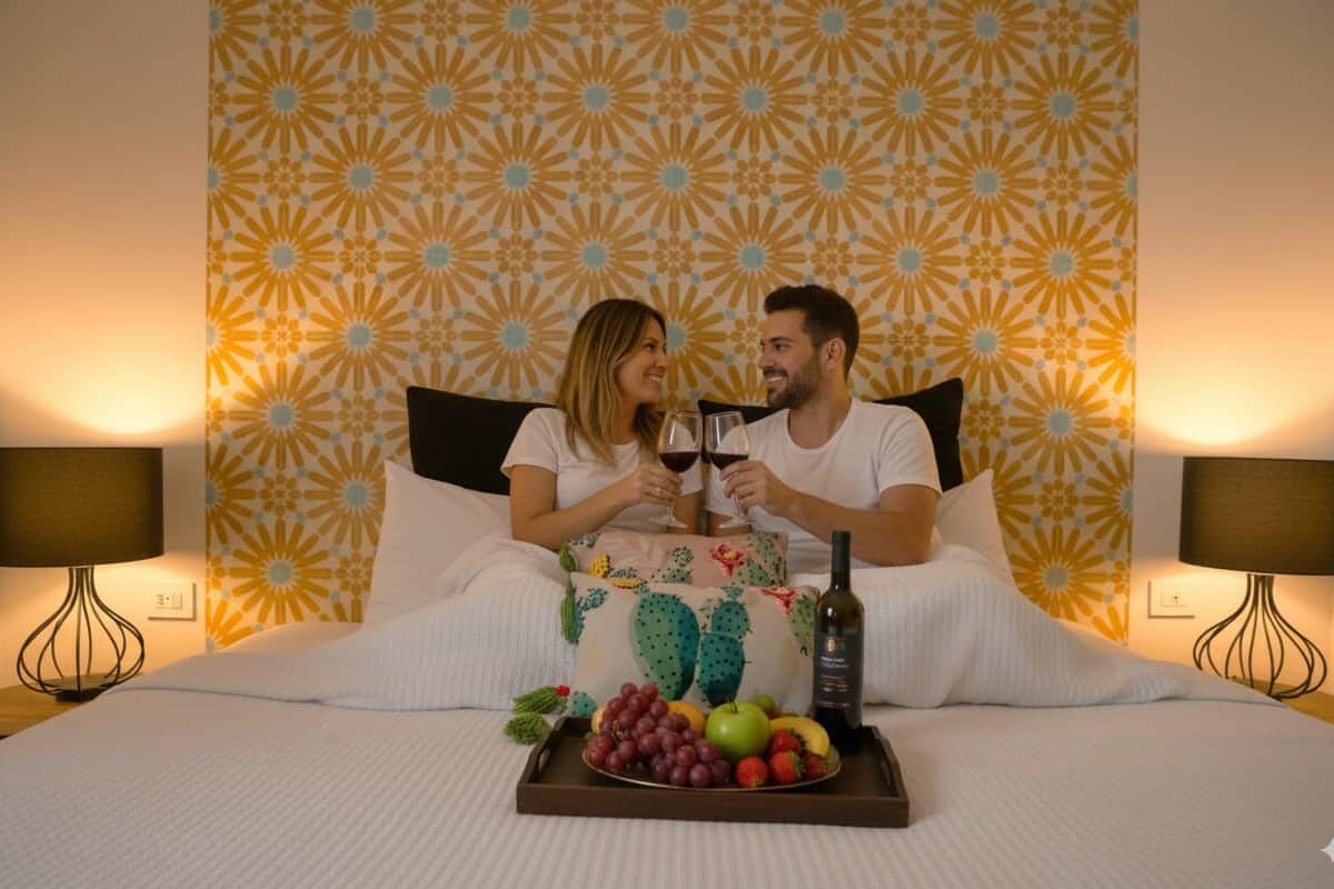 Un couple est assis sur un lit, devant un plateau de fruits et une bouteille de vin.